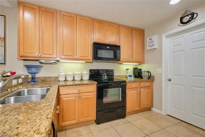 Kitchen with sink, black appliances, light tile patterned floors, and light stone countertops