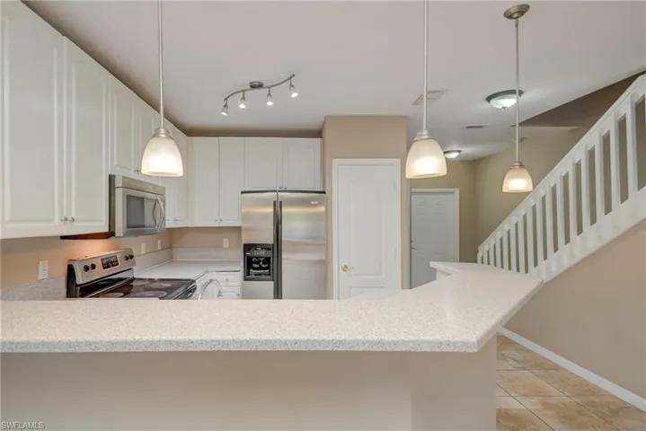 Kitchen featuring stainless steel appliances, decorative light fixtures, white cabinets, a peninsula, and light stone countertops
