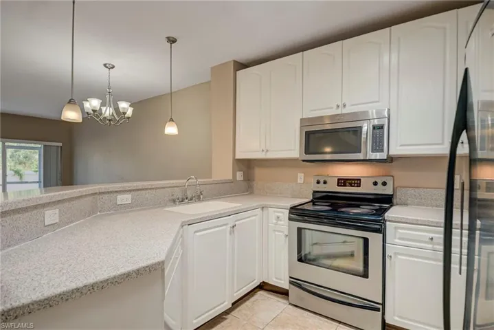 Kitchen with stainless steel appliances, white cabinetry, and hanging light fixtures