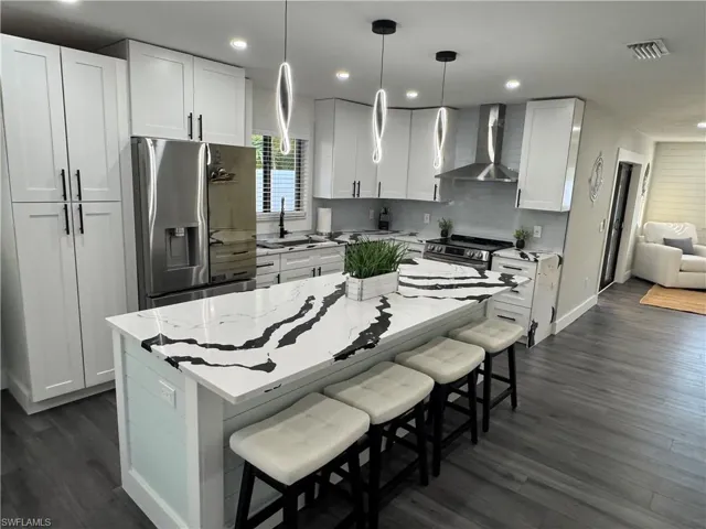 Kitchen with a breakfast bar, white cabinets, stainless steel appliances, light stone counters, and dark wood-style floors