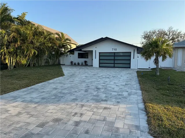 View of front of home with a front lawn, decorative driveway, an attached garage, and stucco siding