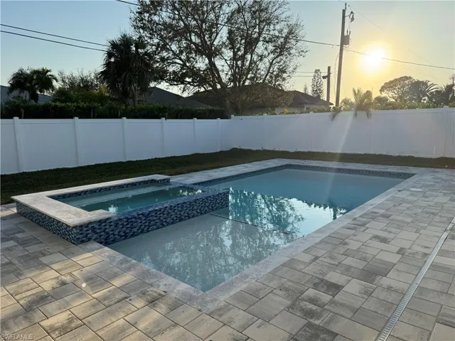 Pool at dusk featuring a pool with connected hot tub, a fenced backyard, and a patio area