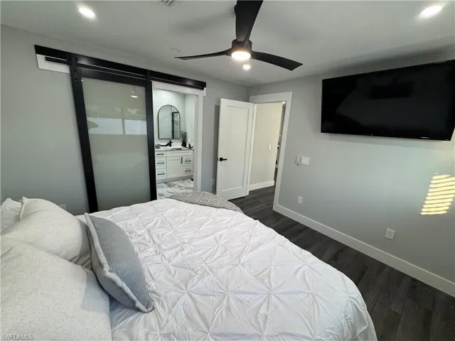 Bedroom featuring dark wood-style flooring, connected bathroom, recessed lighting, ceiling fan, and a barn door