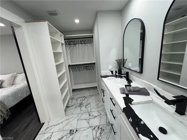 Ensuite bathroom featuring double vanity, light marble finish flooring, recessed lighting, and a walk in closet