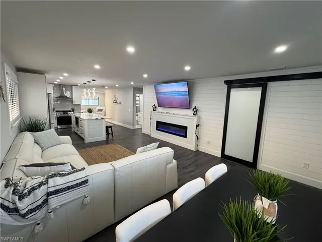 Living room with a glass covered fireplace, dark wood-style flooring, recessed lighting, and wood walls