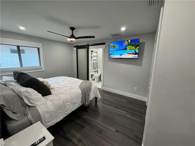 Bedroom featuring dark wood-style floors, a barn door, recessed lighting, ceiling fan, and connected bathroom