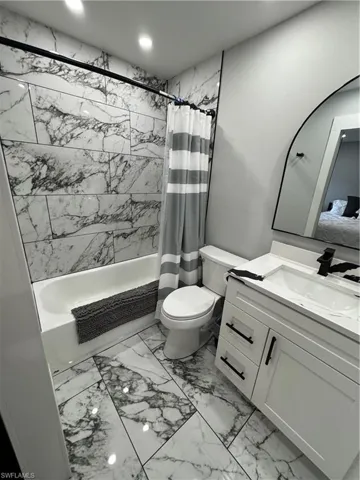 Ensuite bathroom featuring shower / bath combo with shower curtain, vanity, light marble finish floors, and recessed lighting
