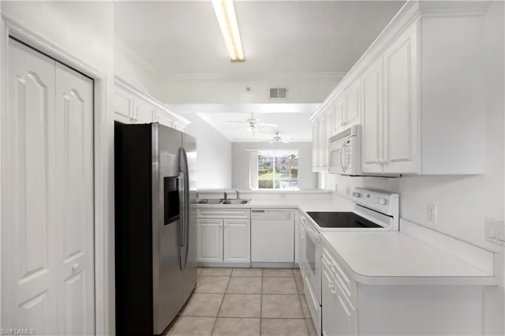 Kitchen featuring white appliances, white cabinetry, light tile patterned flooring, light countertops, and ornamental molding