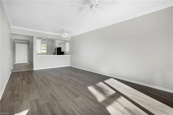 Unfurnished living room featuring crown molding, dark wood-style floors, and a ceiling fan