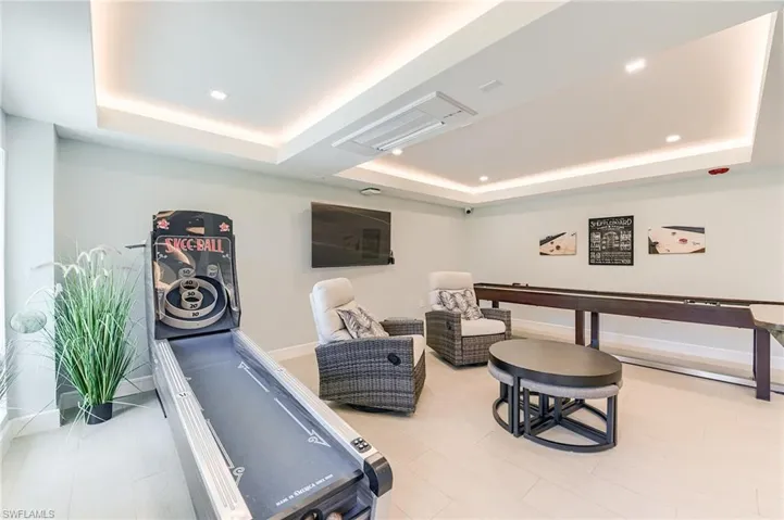 Recessed lighting, tray ceiling, wall-mounted television, shuffleboard table, and light tile flooring