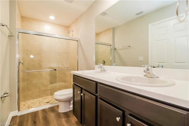 Bathroom with double vanity, a shower stall, and dark wood-style floors