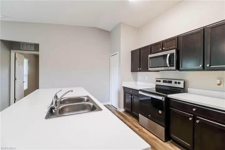 Kitchen featuring stainless steel appliances, light countertops, light wood-style floors, vaulted ceiling, and dark wood finish cabinetry