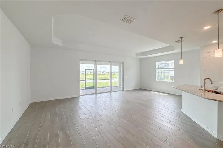Unfurnished living room featuring a tray ceiling, healthy amount of natural light, light wood-style flooring, and recessed lighting