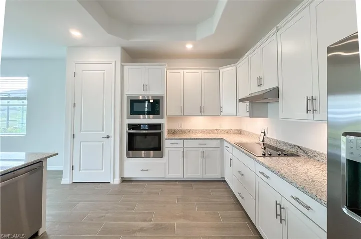 Kitchen with stainless steel appliances, wood finish floors, white cabinetry, light stone counters, and recessed lighting