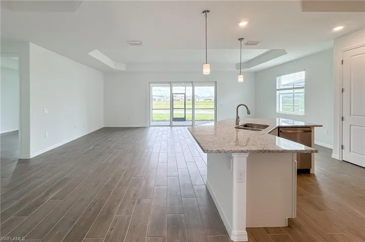 Kitchen featuring a tray ceiling, an island with sink, light stone countertops, pendant lighting, and light wood finished floors