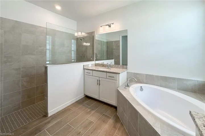 Full bathroom featuring a garden tub, vanity, a walk in shower, and wood finish floors