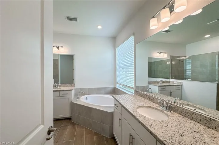 Full bathroom featuring two sinks, vanity, a bath, and walk in shower