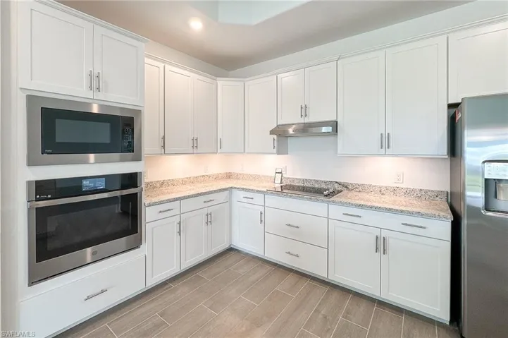Kitchen with stainless steel appliances, white cabinets, light stone counters, wood tiled floors, and under cabinet range hood