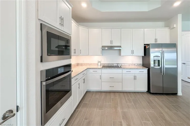 Kitchen featuring appliances with stainless steel finishes, white cabinetry, wood finish floors, a tray ceiling, and under cabinet range hood