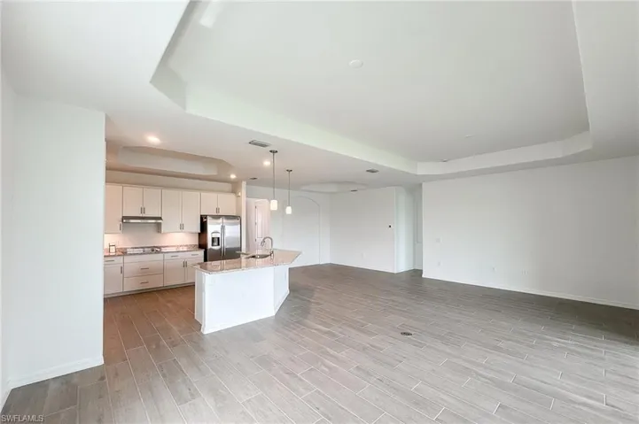 Kitchen featuring a raised ceiling, decorative light fixtures, a kitchen island with sink, light stone counters, and appliances with stainless steel finishes