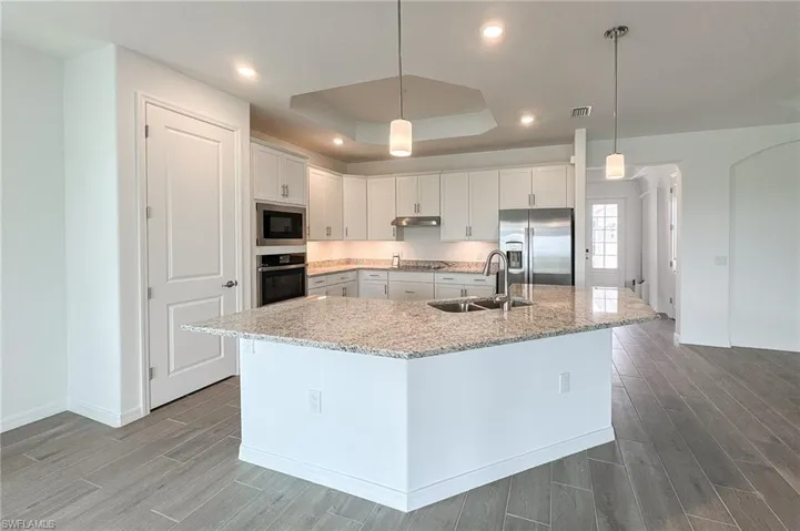 Kitchen featuring wood tiled floors, white cabinetry, light stone countertops, a tray ceiling, and decorative light fixtures