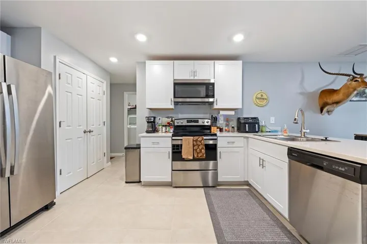 Kitchen featuring appliances with stainless steel finishes, white cabinetry, recessed lighting, light tile patterned floors, and a peninsula