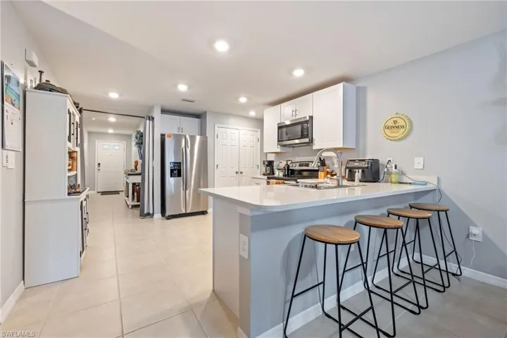 Kitchen with a kitchen bar, a peninsula, stainless steel appliances, white cabinets, and recessed lighting