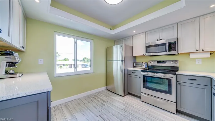 Kitchen with a tray ceiling, gray cabinets, stainless steel appliances, recessed lighting, and light stone countertops