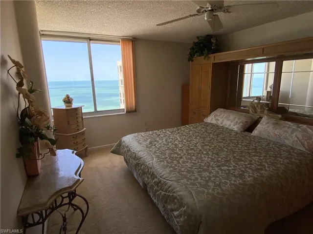 Bedroom featuring ceiling fan, a water view, carpet flooring, and a textured ceiling