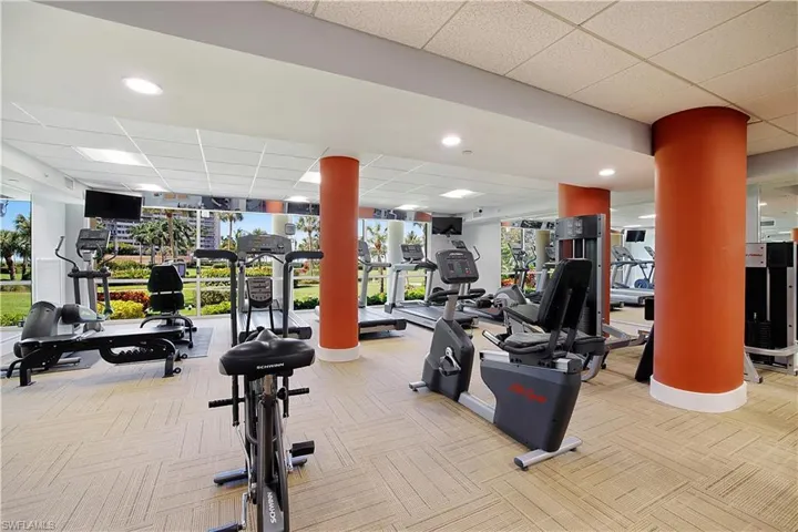 Gym featuring a drop ceiling, decorative columns, and light colored carpet
