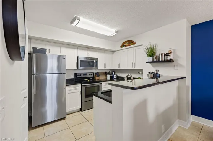 Kitchen featuring appliances with stainless steel finishes, white cabinetry, light tile floors, and kitchen peninsula