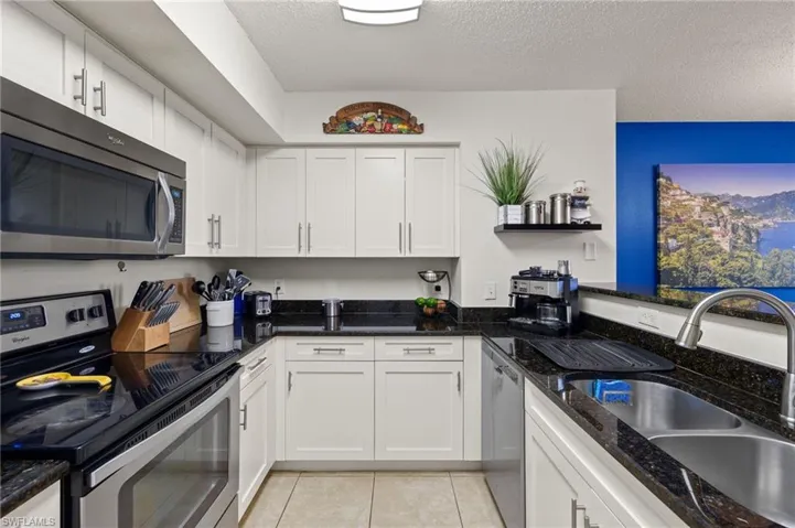 Kitchen featuring white cabinetry, stainless steel appliances, granite counters, sink, and light tile floors