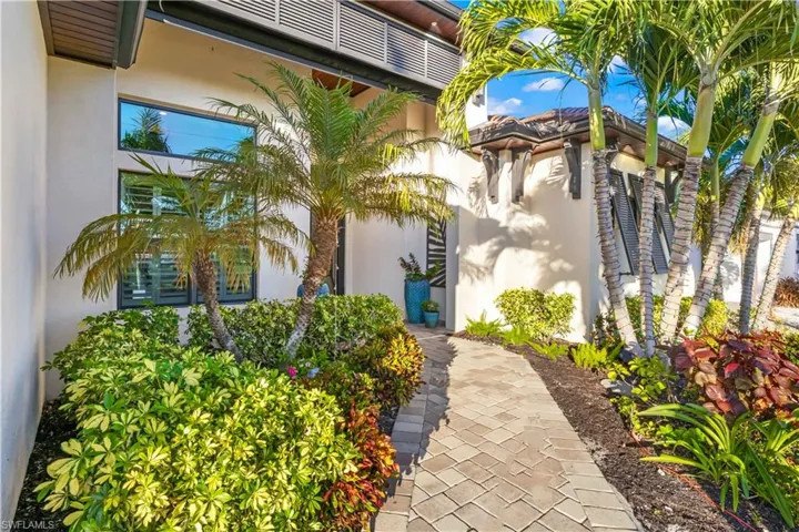 Inviting front entrance framed by Bahama shutters, lush landscaping and pavered walkways, creating a welcoming first impression.