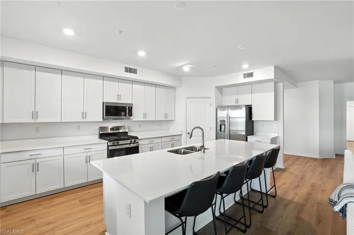Kitchen with appliances with stainless steel finishes, a kitchen breakfast bar, light wood finished floors, a kitchen island with sink, and recessed lighting