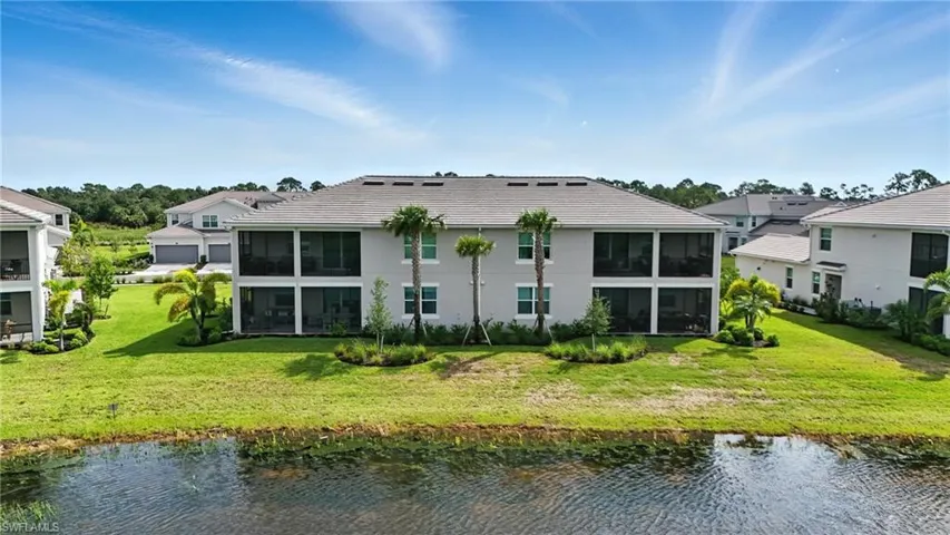 Rear view of house featuring a sunroom, a water view, and a lawn