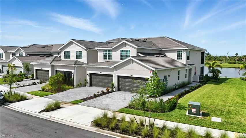 View of front facade with a tile roof, an attached garage, driveway, a front yard, and stucco siding