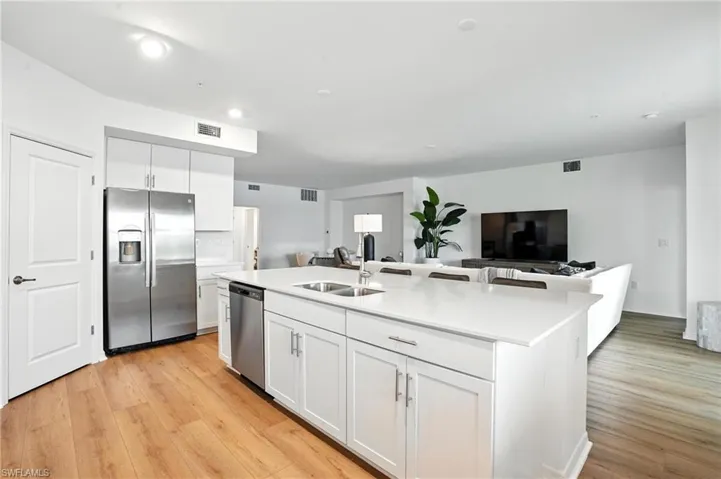 Kitchen with appliances with stainless steel finishes, white cabinets, light wood-type flooring, a center island with sink, and light countertops