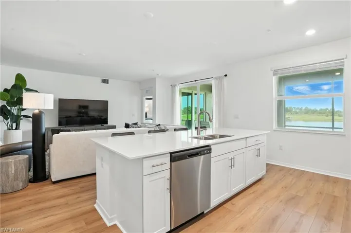 Kitchen with stainless steel dishwasher, light wood finished floors, open floor plan, a kitchen island with sink, and white cabinetry