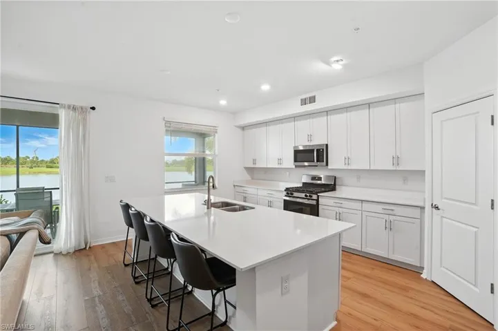 Kitchen with appliances with stainless steel finishes, a center island with sink, a breakfast bar, light wood-style floors, and white cabinetry