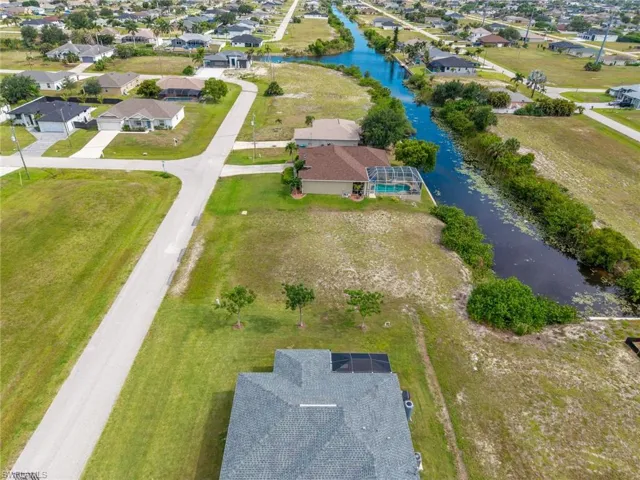 Canal-front property featuring a single-story home with a screened pool enclosure and adjacent undeveloped land