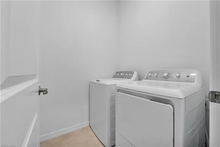 Clothes washing area with washing machine and dryer and light tile floors