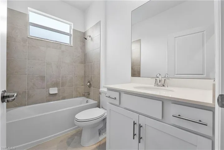 Full bathroom with tile floors, toilet, vanity, and tiled shower / bath