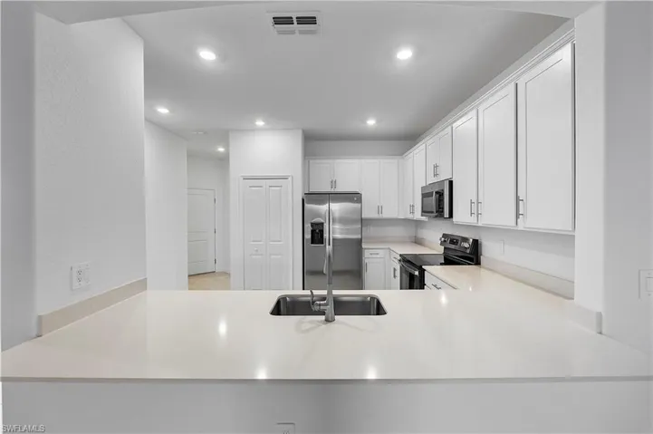 Kitchen with sink, kitchen peninsula, white cabinetry, and appliances with stainless steel finishes
