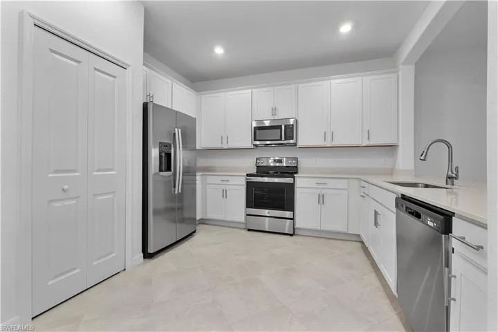 Kitchen with stainless steel appliances, sink, white cabinetry, and light tile floors