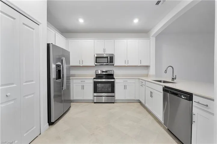 Kitchen featuring appliances with stainless steel finishes, white cabinetry, sink, and light tile floors