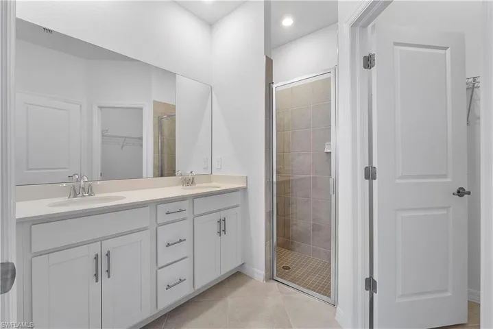 Bathroom with a tile shower, double sink, tile floors, and vanity with extensive cabinet space