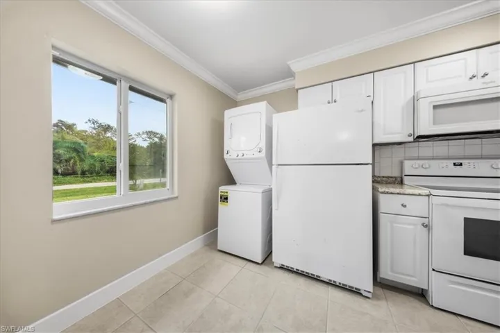 Second Unit-Kitchen featuring white appliances, estacked washer and dryer, ornamental molding, decorative backsplash, and white cabinets