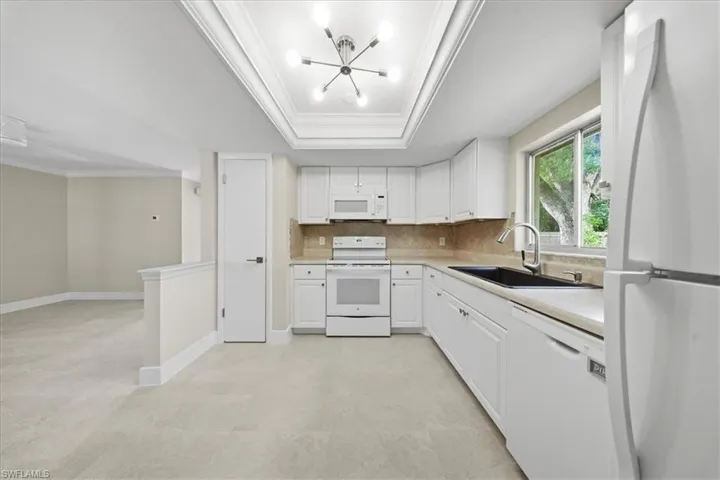 Kitchen featuring white appliances, light countertops, crown molding, a chandelier, and white cabinetry