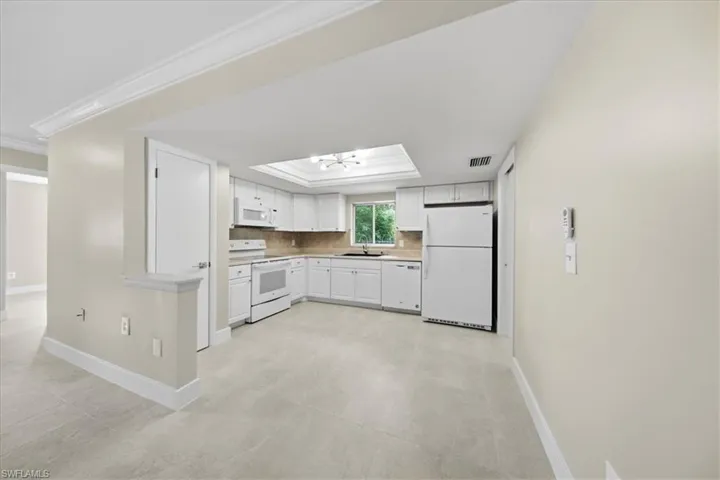 Kitchen with white cabinets, white appliances, light countertops, ornamental molding, and a tray ceiling