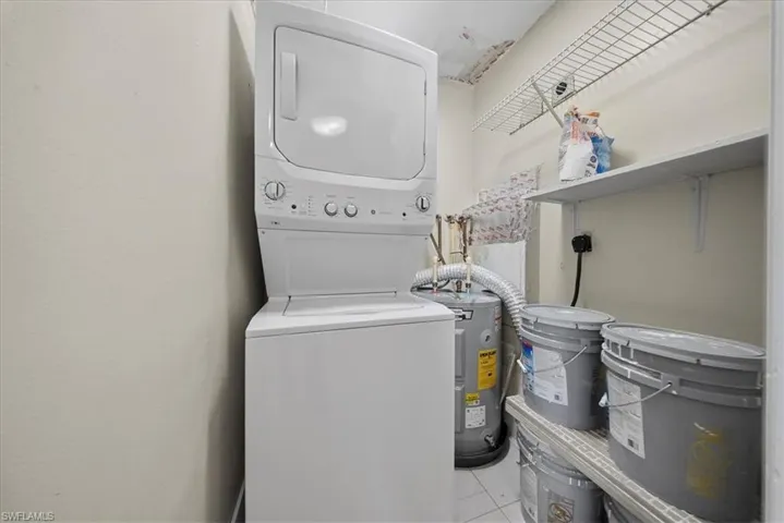 Washroom featuring estacked washer and dryer, light tile patterned flooring, and electric water heater